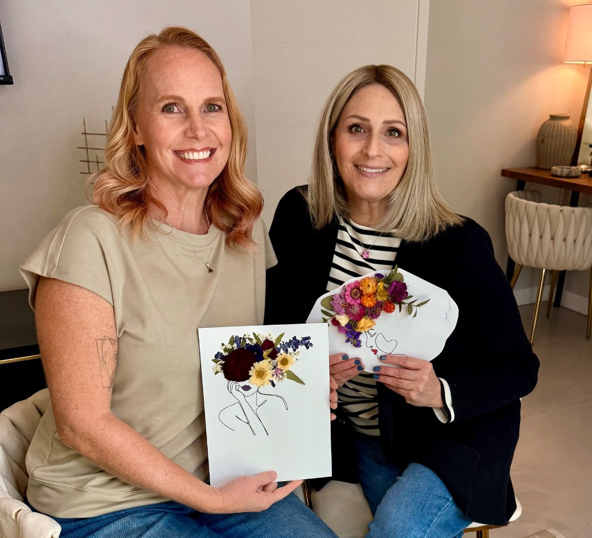 Kaycee, with red hair, and Joclynn, with blonde hair, seated together holding pressed-flower art pieces