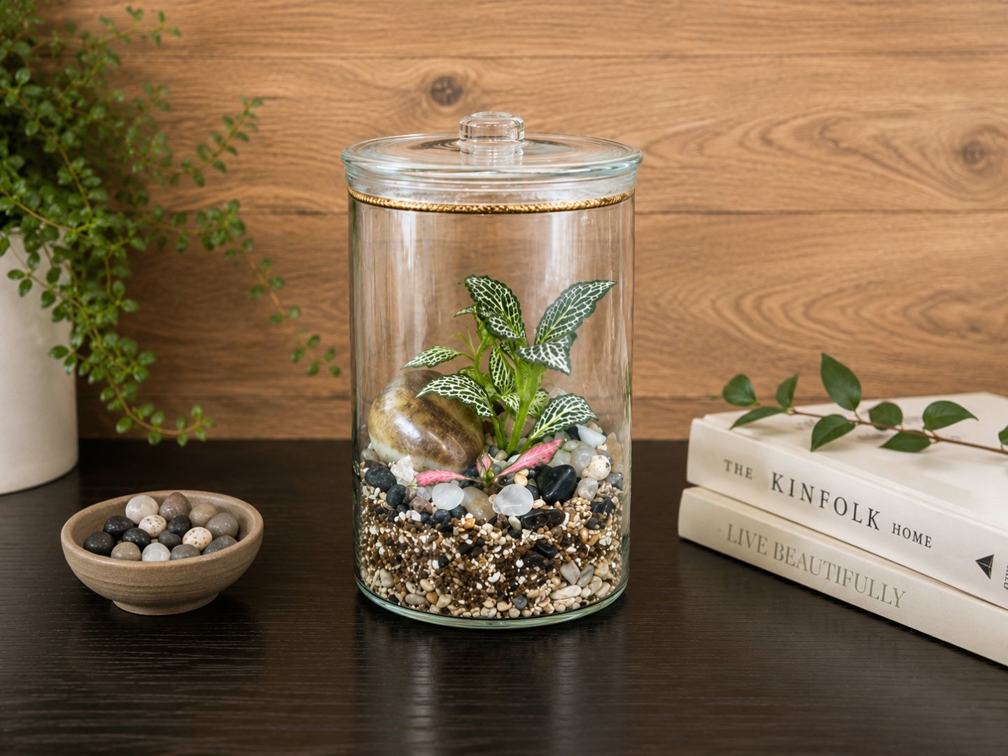 A layered glass terrarium with moss, pebbles, and a small fittonia plant